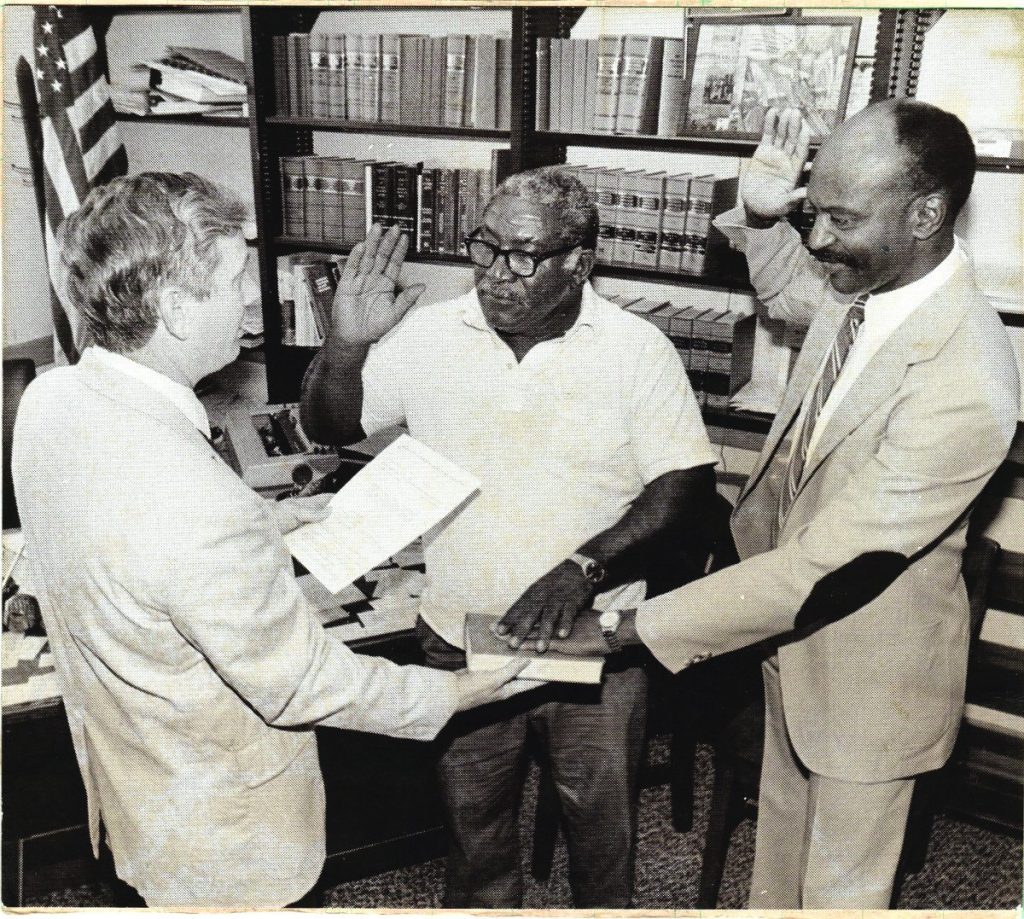 A black and white photo with Probate Judge Dan Coward swearing in Mr. Frank Moody (left) and Coach Willie Batchelor (right) as Cook County's first Black elected official positions.