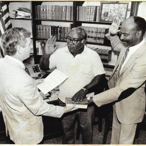 A black and white photo with Probate Judge Dan Coward swearing in Mr. Frank Moody (left) and Coach Willie Batchelor (right) as Cook County's first Black elected official positions.
