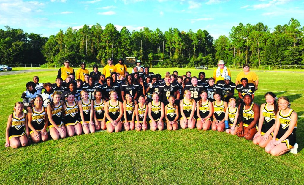 The CMS Hornets football team, cheerleaders, and coaches, pose for a picture in a vibrant green field.