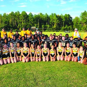 The CMS Hornets football team, cheerleaders, and coaches, pose for a picture in a vibrant green field.