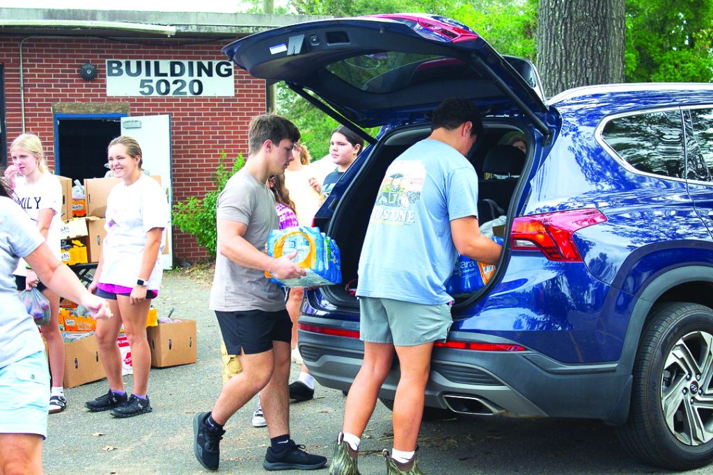 Two teenage boys load cases of water into the back of a blue SUV.