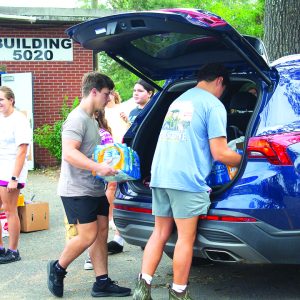 Two teenage boys load cases of water into the back of a blue SUV.
